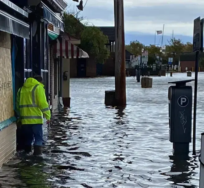 Worker in a safety jacket wading through storm flood water on a street