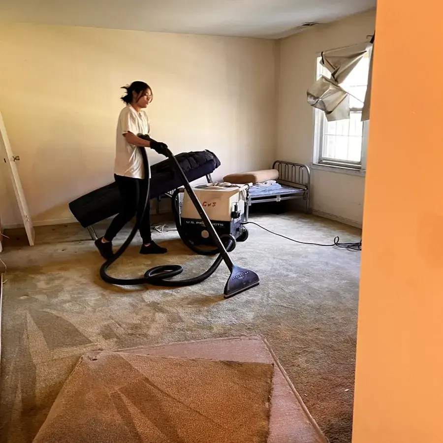 Technician running an extraction wand over soaked carpet in a bedroom