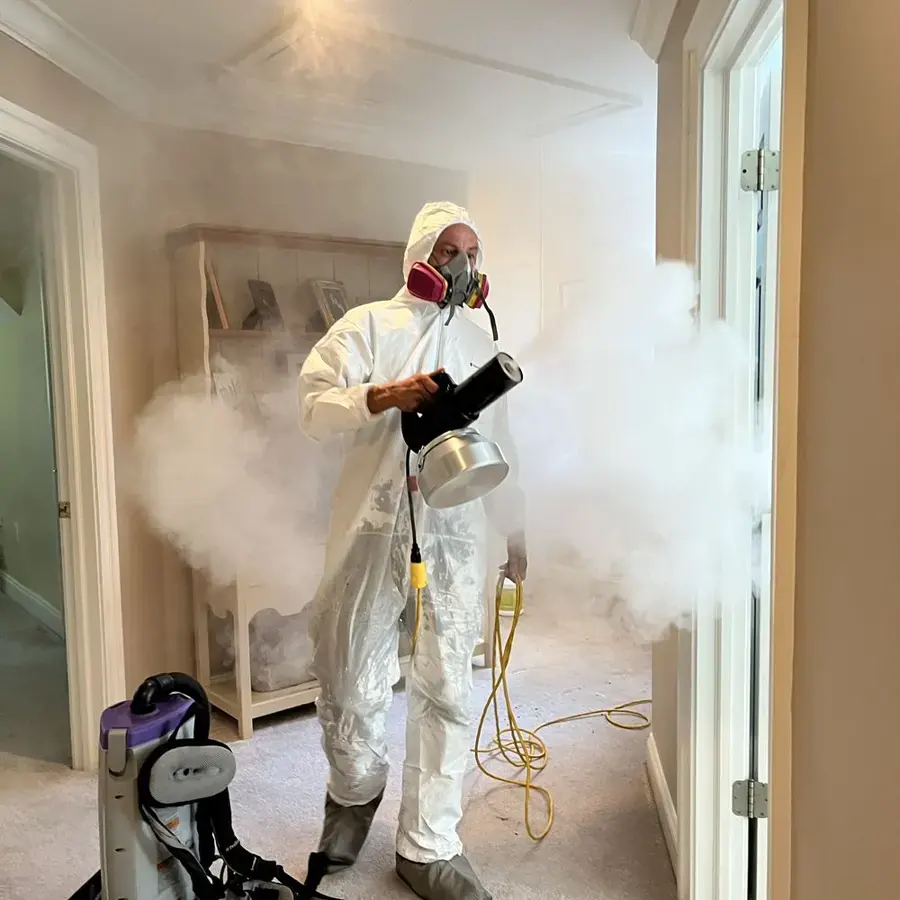 Technician in a protective suit and respirator fogging antimicrobial in a hallway
